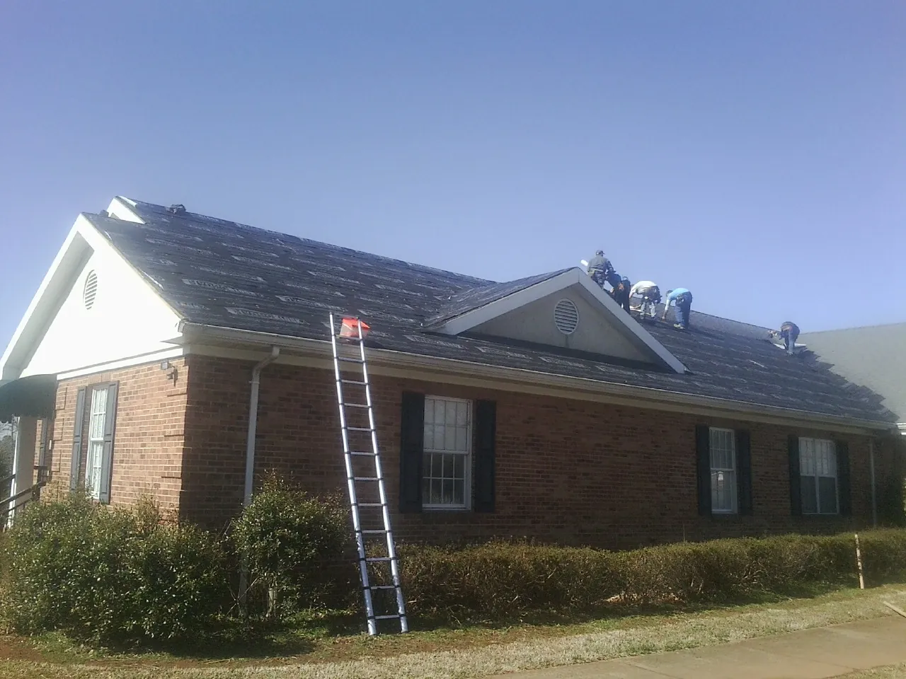 Crew tearing shingles off a brick ranch roof with a ladder set — Metal Roof Repair work by our crew in Forest City