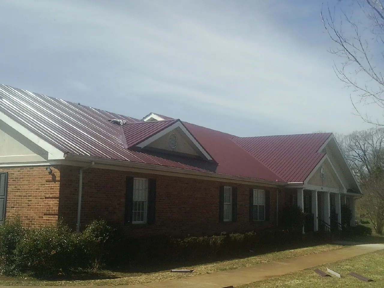Red metal roof with gabled entries on a long brick building, from a Hail Damage Roof Repair job in Forest City