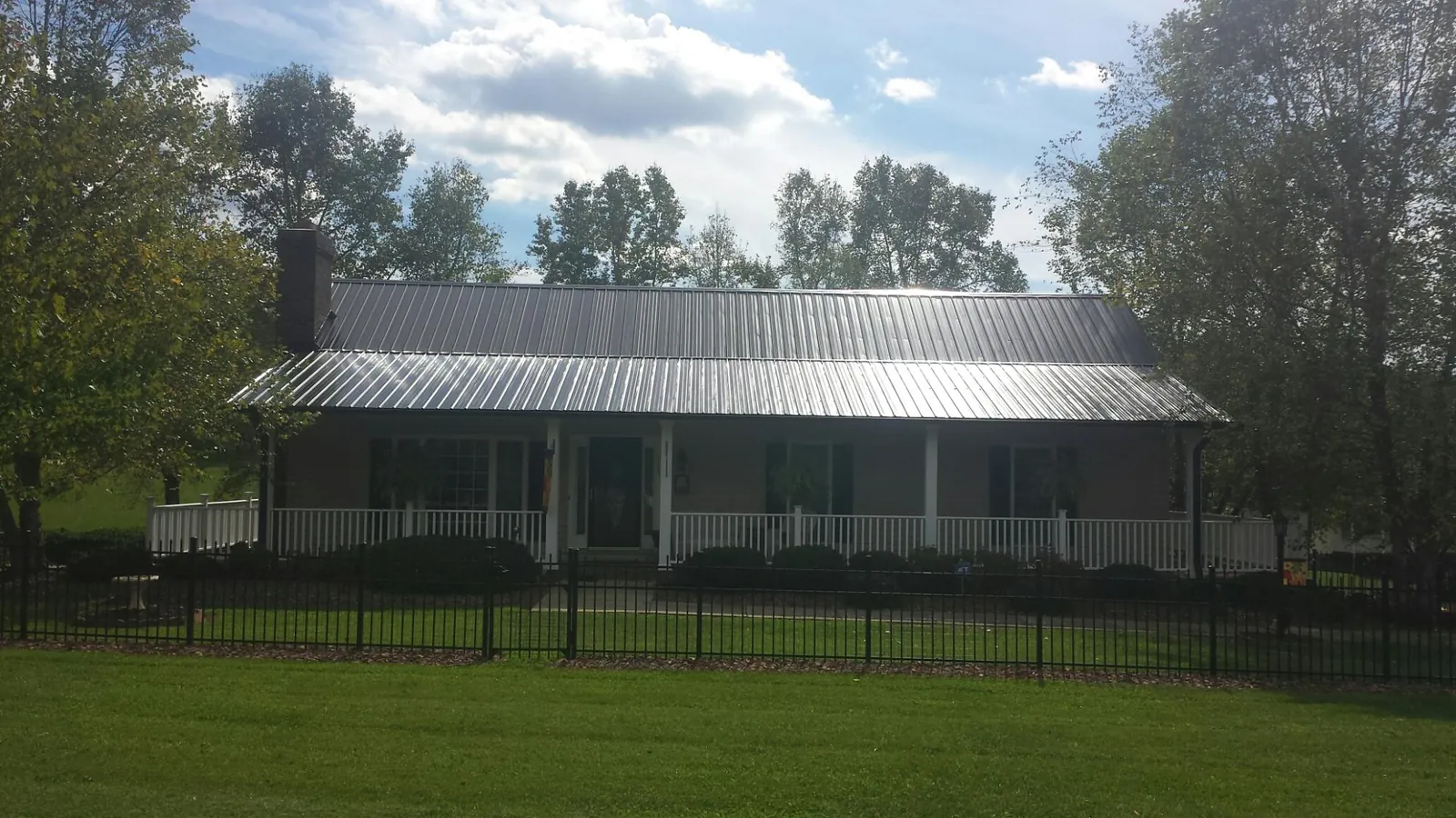 Gray metal roof on a brick ranch with a full width front porch — Gutter Guard Installation work by our crew in Forest City